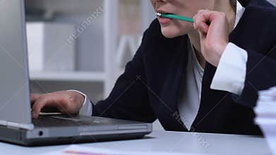 Woman working on laptop and chewing pencil, bad habit from stressful job closeup
