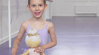 Cute happy little ballerina girl smiling joyfully holding ballerina doll
