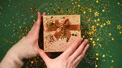 Woman hands opening gift box. Sparkling gold stars, glitter confetti over present. Unpacking gift on green background