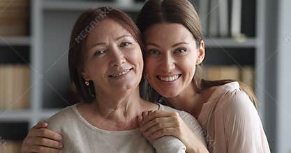 Beautiful adult daughter hugging older mature mum looking at camera