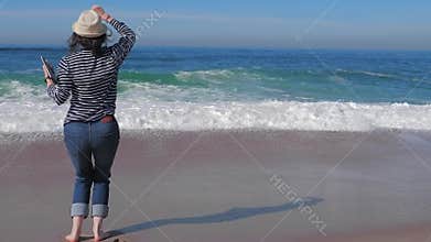 Happy woman running and jumping on the beach with laptop in straw hat