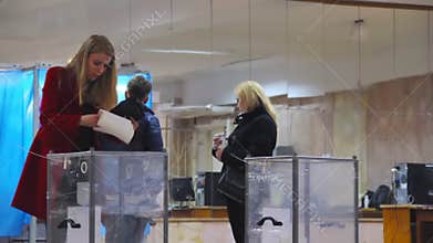 Young female blond voter puts the ballot in ballot box.