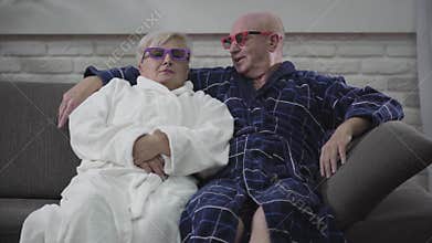 Cheerful caucasian senior couple sitting on sofa and moving depending on 3D movie. Joyful husband and wife resting at