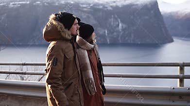 Tourists in winter coats and black hats walking in slow motion on a long road through the countryside towards the snowy