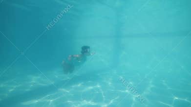 Active brave little girl swimming underwater in pool.