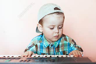 Portrait of a pretty boy wearing baseball cap backwards playing the digital piano