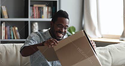 Excited african male customer receiving opening parcel box at home