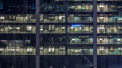 Office building exterior during late evening with interior lights on and people working inside night timelapse