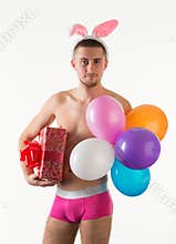 Young man in pink mens underpants standing and holding present box and balloons