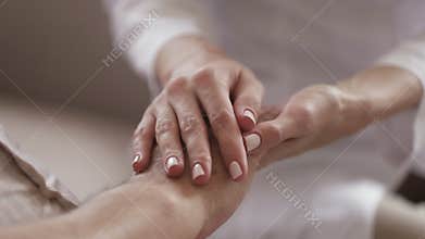 Young woman caregiver holding hand of old man, closeup view