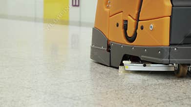 Orange automatic professional floor cleaning machine riding on the floor at shopping mall. Floor care and cleaning