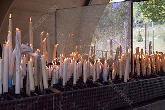Big burning candles from prayers for hope. Saint Bernadette grotto with many white candles with flame. Sanctuary in Lourdes.