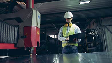 Factory employee is watching laser equipment cutting metal. Professional heavy Industry Engineer.
