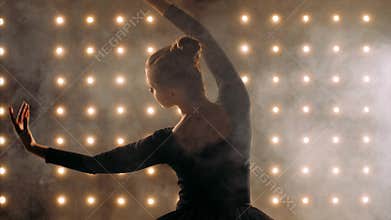 Silhouette of ballerina in black dress is dancing ballet in the dark studio.