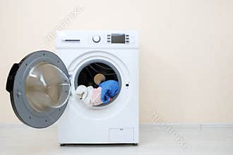 Washing machine with laundry in drum near beige wall