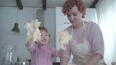 Little daughter helps mom in the kitchen with baking. Knead the dough together