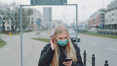 Coronavirus pandemic: blonde woman in a medical mask writing message on smartphone