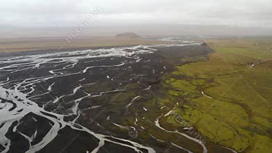 Aerial view of glacial rivers, river delta, black volcanic sand in south Iceland,  a green plain and a mountain in the distance, c