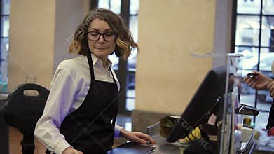 Smiling female cashier in black apron and unrecognizable customer paying with her EC card at supermarket checkout and