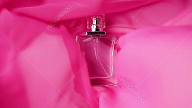 Flat surfaced bottle with cyan perfumes or essential oils is on the pink cloth. Pink fabric flutters around and waves around