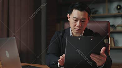 Gentleman revising info between papers and laptop in office