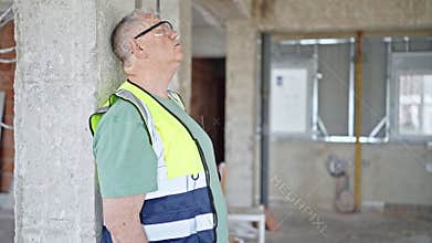 Middle age grey-haired man builder leaning on wall tired at construction site