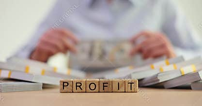 Woman banker counts money at table with word Profit