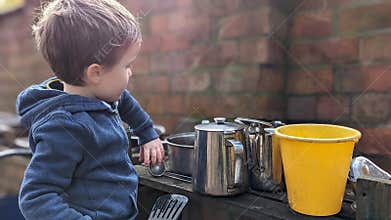 A boy playing with a mud outdoor kitchen holding utensils