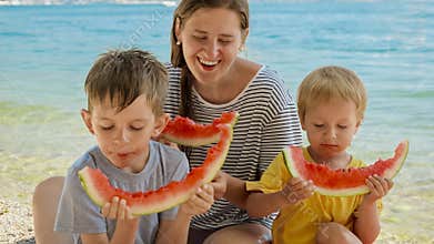 Mother and her two boys enjoy sweet watermelon on a beachside picnic. Family bonding during a holiday, summertime