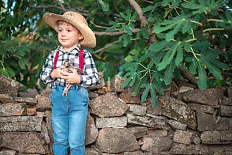Happy kid boy little farmer holds a newborn baby chicken in his hands outdoor in the farm. Farm animals and farmland