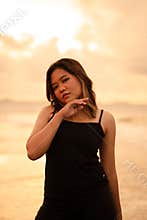 An Asian woman with brown hair and black clothes makes sexy poses very skillfully while enjoying the beach