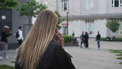Back view unrecognizable blonde caucasian woman walking outdoors near office building talking on mobile phone successful
