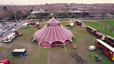 Red circus tent seen from aerial perspective standing on a grass field next to car parking lot. Entertainment concept.