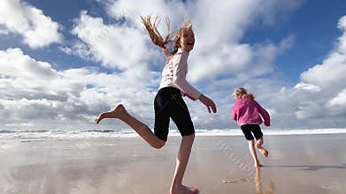 Children run along the coast of the Atlantic Ocean. Two little sisters are playing with the waves on the beach of the