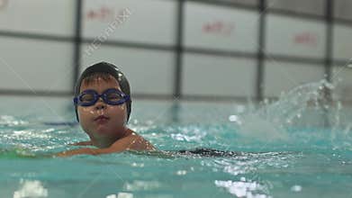 low angle swimming child boy face in swimming goggles and cap, kid diving into water indoor pool breathes under water