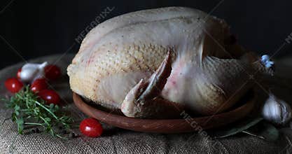 Whole raw chicken broiler in wooden plate with red cherry tomatoes still life