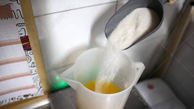 Worker at food factory pouring sugar from scoop to a mixing bucket with cold freshly squeezed orange juice for ice cream