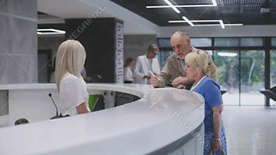 Elderly couple stand near reception desk in clinic