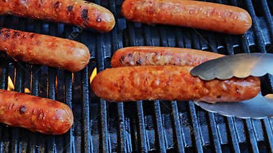 Grilled sausages Bockwurst on barbecue grill grate, flame. Turn the sausages over. Close up. Slow motion.