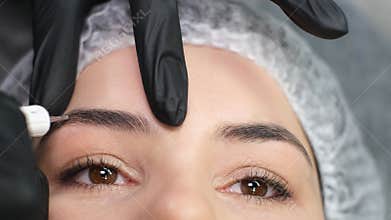 Cosmetician in gloves making permanent brow makeup to a woman at beauty salon. Closeup.
