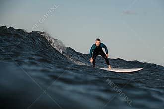 Handsome young male surfer standing on a surfboard in the middle of the sea