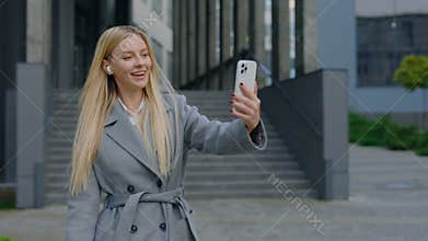 Cute Blonde Young Businesswoman Making Online Video Chat Conference with Clients, Using Smartphone While Walking Outside