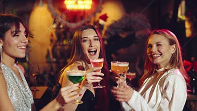 Merry holidays. Happy, beautiful, smiling young girls meeting in bar to celebrate, drinking cocktails and dancing