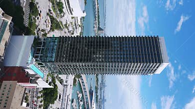 Vertical video of stylish multistorey building rising up against Miami harbor scenery. Wide view of appealing super-tall
