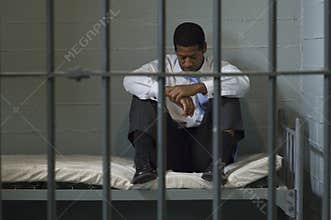 Man Sitting On Bed In Prison Cell