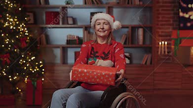 Smiling Senior Woman on Wheelchair Showing and Holding New Year Present to Camera. Elderly Disabled Lady Sitting on