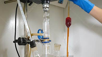 Laboratory in chemical plant. Scientist sampling chemical extract from round glass flask with tubes. Boiling liquid