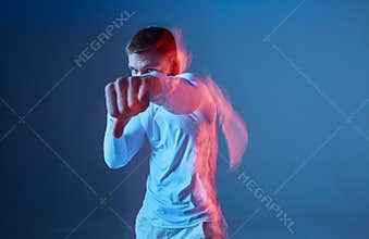 Male athlete does left kick, he wears white sportswear on blue background. Boxer punches, hits, beats.