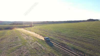 Pickup truck driving along road near field with sunlight at background. Black car moving on route at countryside. Off