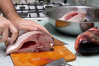 Man prepares fresh silver carp fish. Cuts it into steaks with a knife. home cooking concept